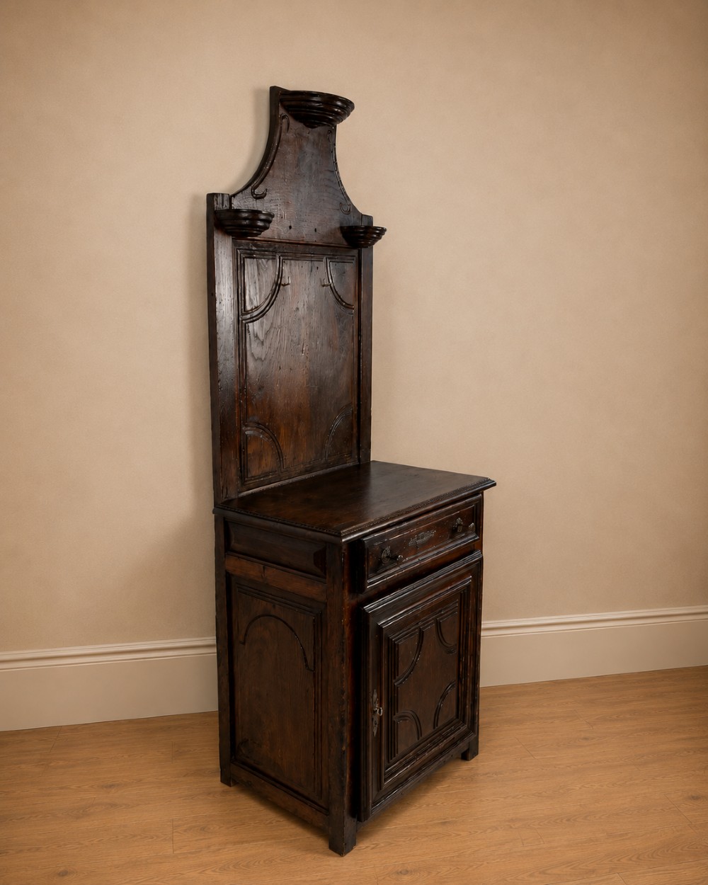 An 18th-century dark chestnut wood lavabo cabinet featuring a carved backboard mounted with a pewter cistern above a matching pewter basin. View XV