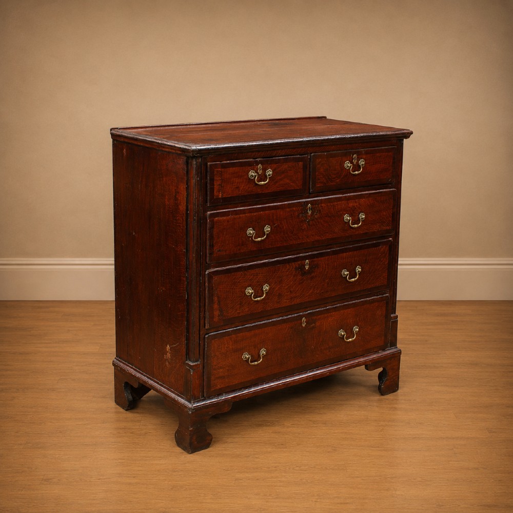 A Georgian dark oak chest of drawers featuring two short drawers over three long drawers with mahogany crossbanding and brass swan-neck handles. View II