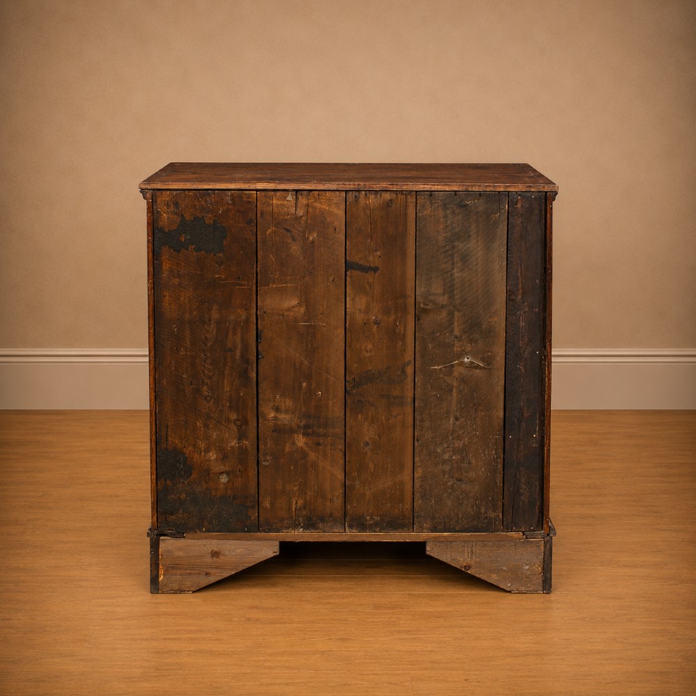 A Georgian dark oak chest of drawers featuring two short drawers over three long drawers with mahogany crossbanding and brass swan-neck handles. View V