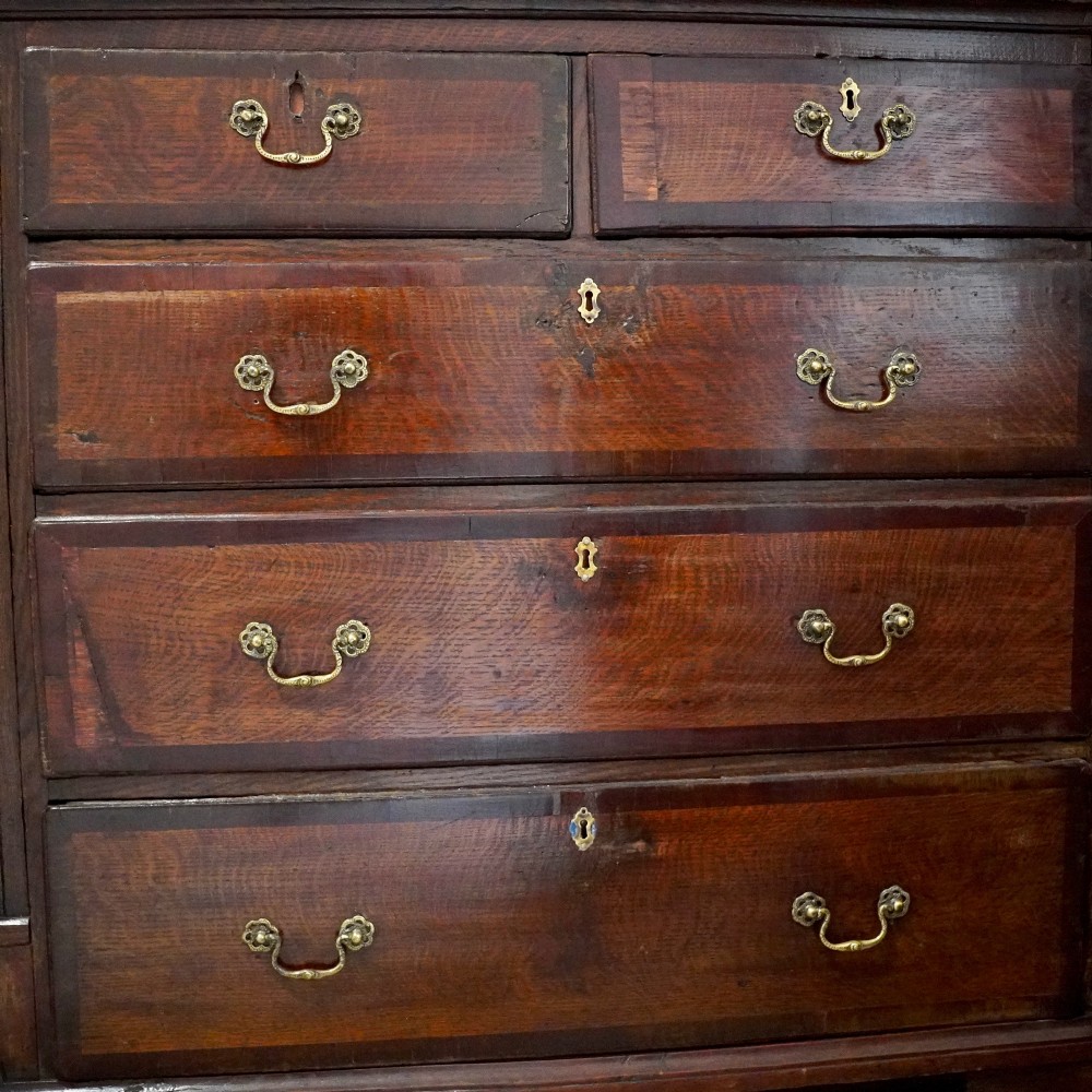 A Georgian dark oak chest of drawers featuring two short drawers over three long drawers with mahogany crossbanding and brass swan-neck handles. View VI