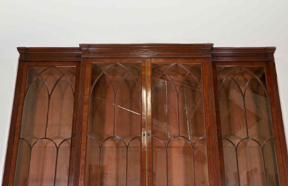 A large George IV mahogany breakfront library bookcase featuring gothic astragal glazed upper doors above drawers and cupboard doors with geometric moulding. View VIII