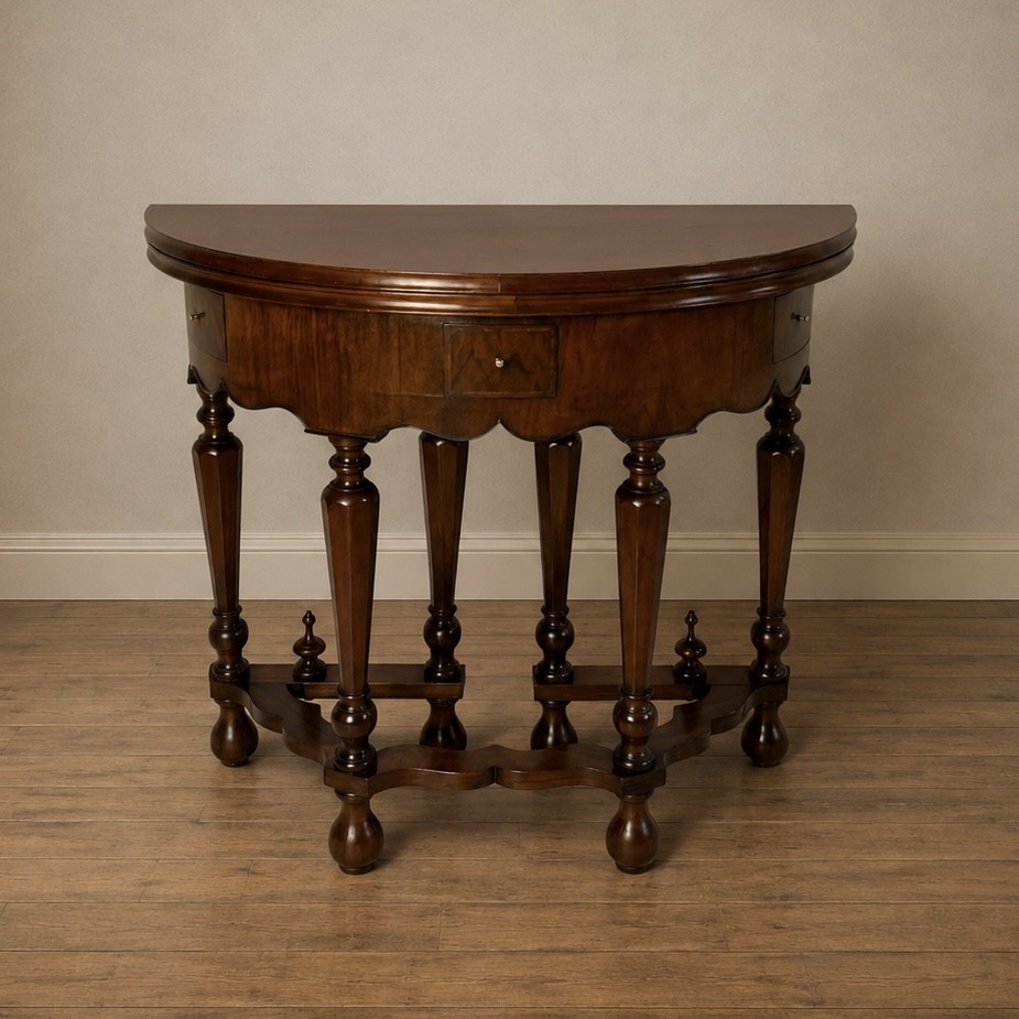 A Victorian figured walnut demi-lune card table featuring a scalloped apron, small frieze drawers, multiple turned legs, and a shaped stretcher base.