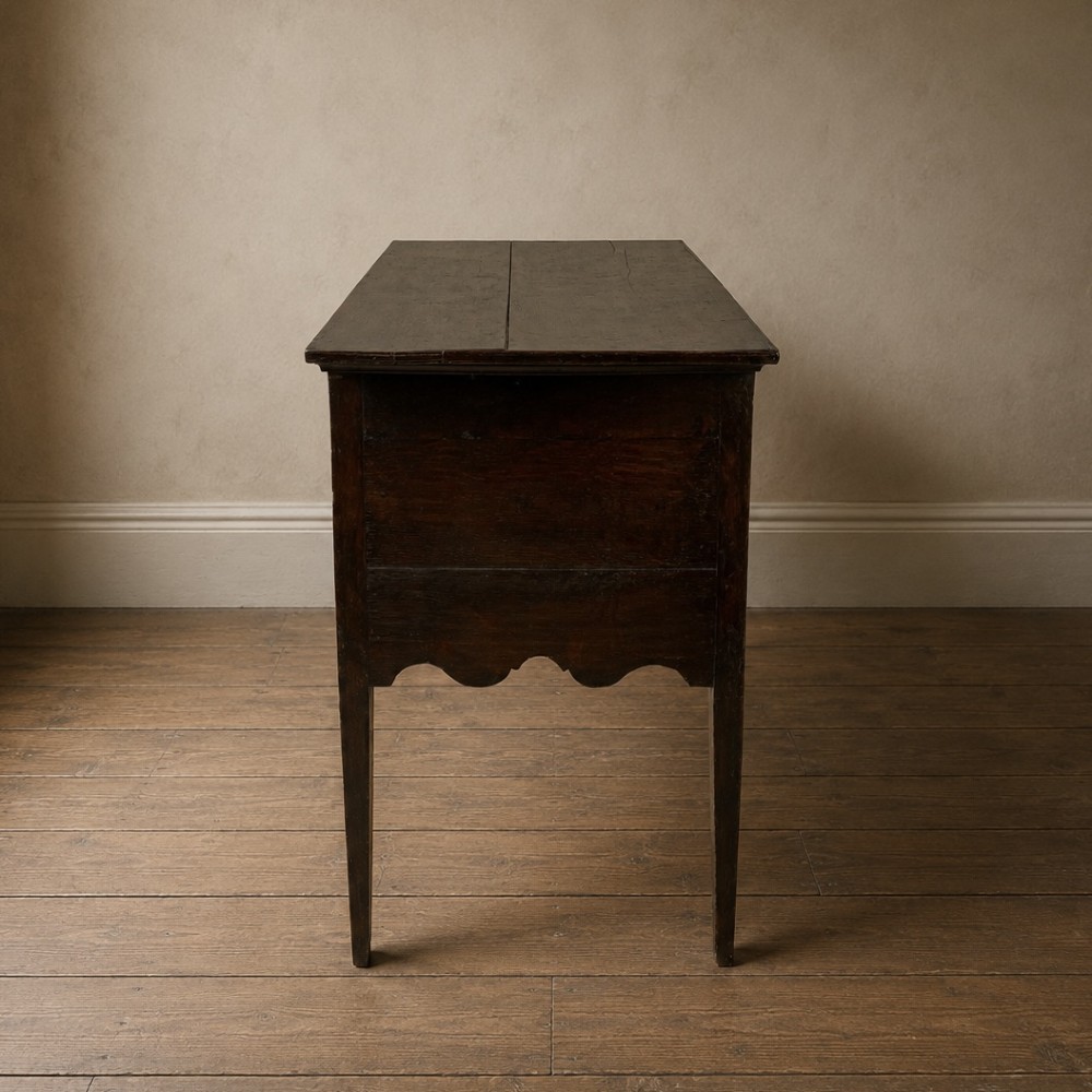 An 18th-century Georgian dark oak lowboy side table featuring three drawers with brass handles, a shaped apron, and slender square legs. View V
