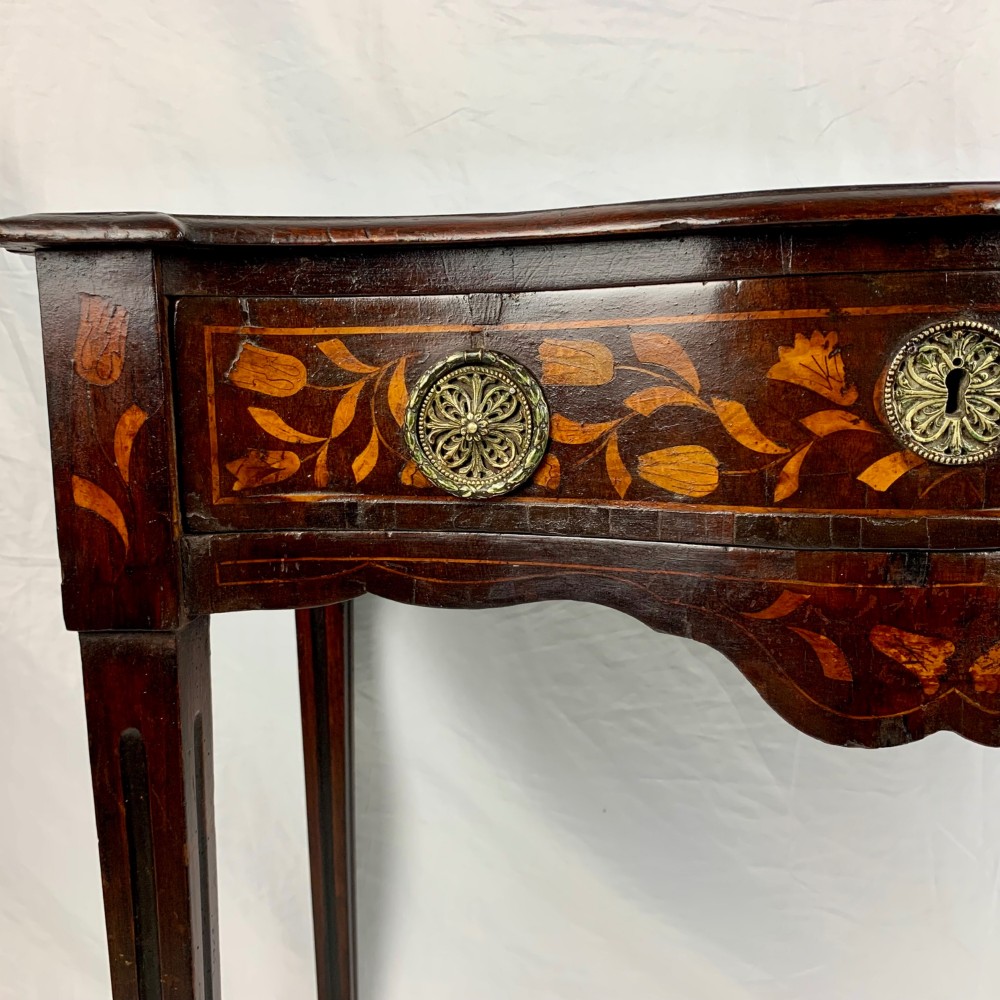 An 18th-century Dutch walnut side table featuring a serpentine front, floral marquetry inlay, a single drawer, and four square tapered legs. View IX