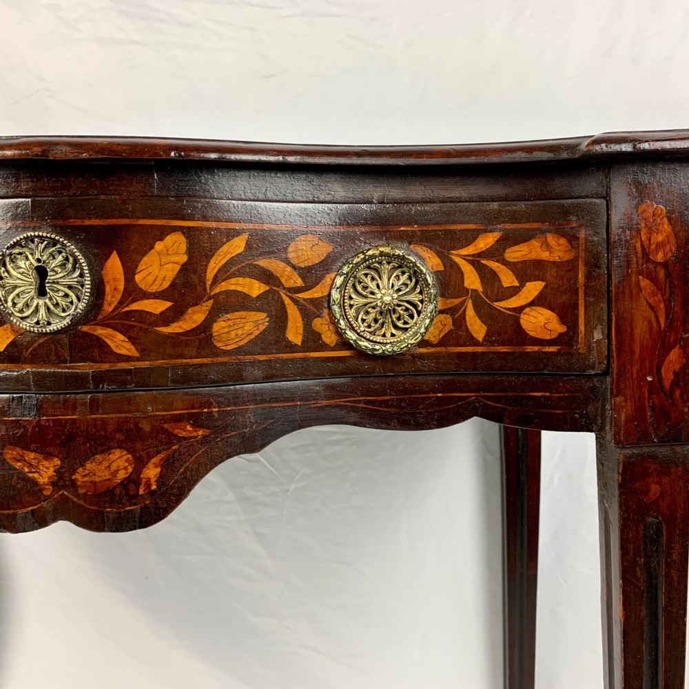 An 18th-century Dutch walnut side table featuring a serpentine front, floral marquetry inlay, a single drawer, and four square tapered legs. View X