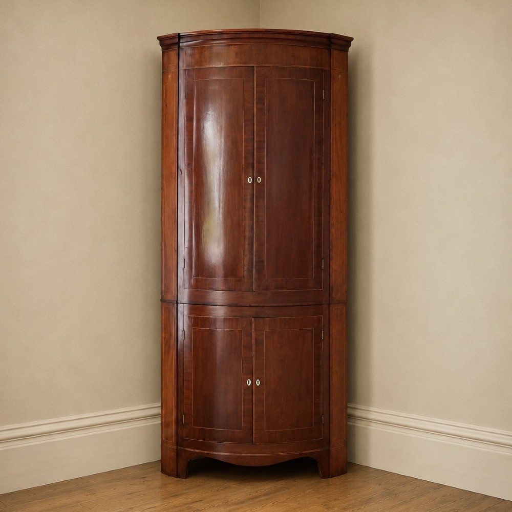 A tall Georgian mahogany bowfront corner cupboard featuring two upper curved doors, two lower curved doors, and fine line inlay.