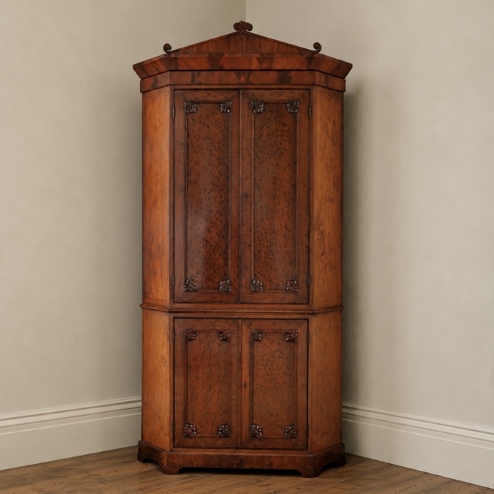 A tall, two-tier William IV corner cupboard crafted from dark plum pudding mahogany, featuring panelled double doors on both top and bottom sections with carved detail and a pediment top.
