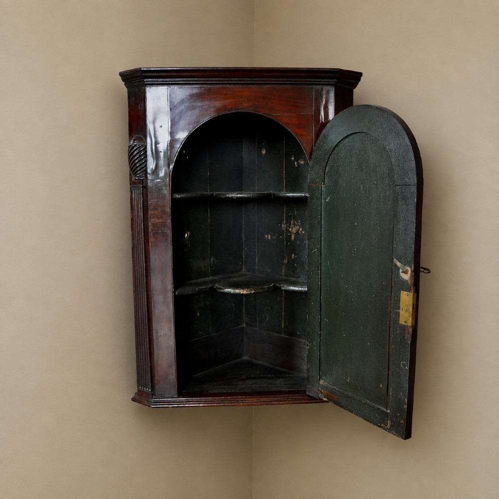 Mid-18th century Georgian mahogany hanging corner cupboard featuring an arched panelled door, brass hardware, and fluted pilasters. View XI