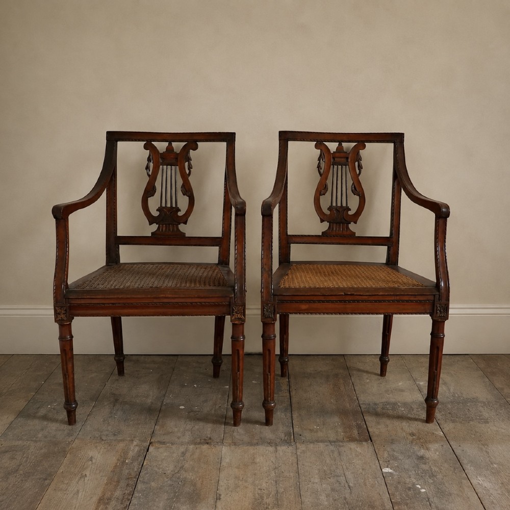 A matching pair of 19th-century Regency style mahogany armchairs featuring carved lyre back splats and woven cane seats.