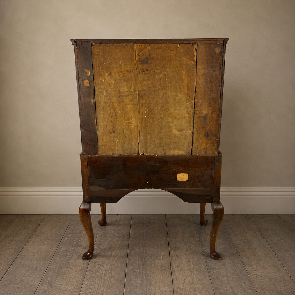 An early 18th-century Queen Anne walnut chest on stand featuring crossbanded drawers, brass teardrop handles, and cabriole legs. View XV