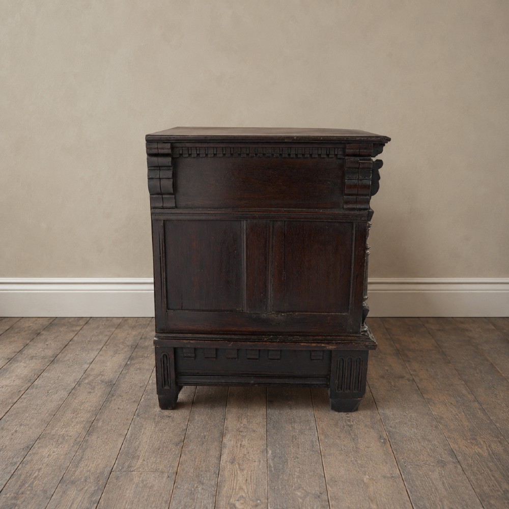 A dark oak 17th-century style chest of drawers featuring geometric timber inlay along the top frieze, applied mouldings, and brass drop handles. View XIV