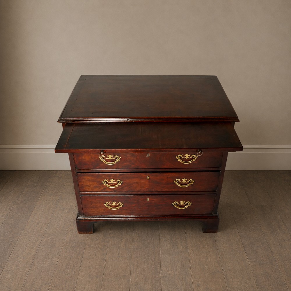 A George III flame mahogany bachelors chest of drawers featuring four graduated drawers, a pull-out brushing slide, ornate brass handles, and bracket feet. View XV