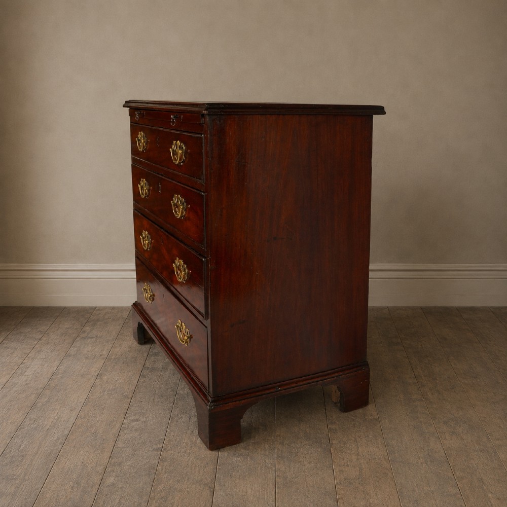 A George III flame mahogany bachelors chest of drawers featuring four graduated drawers, a pull-out brushing slide, ornate brass handles, and bracket feet. View XVI