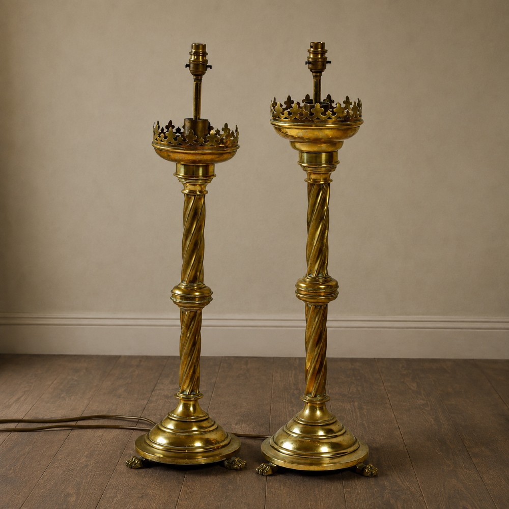 A pair of 19th-century converted brass altar candlesticks with spiral columns, pierced crown drip pans, and cast paw feet.