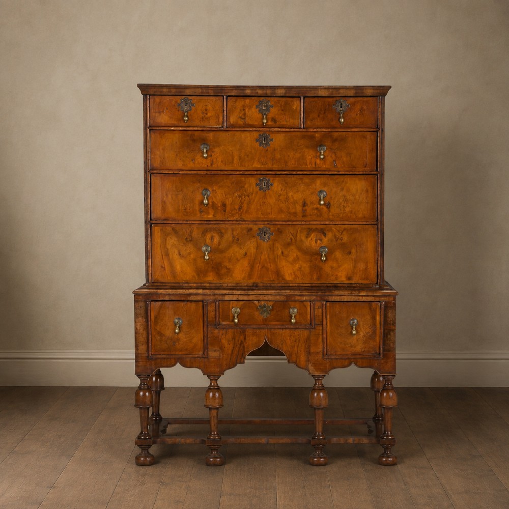 An early eighteenth-century Queen Anne walnut chest on stand featuring multiple drawers, brass teardrop handles, a shaped apron, and turned legs connected by stretchers.