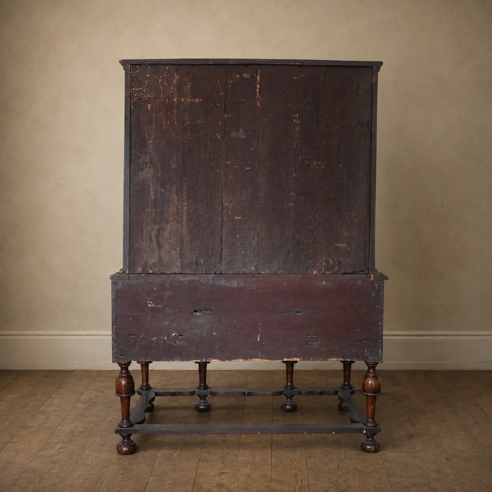 An early eighteenth-century Queen Anne walnut chest on stand featuring multiple drawers, brass teardrop handles, a shaped apron, and turned legs connected by stretchers. View XV