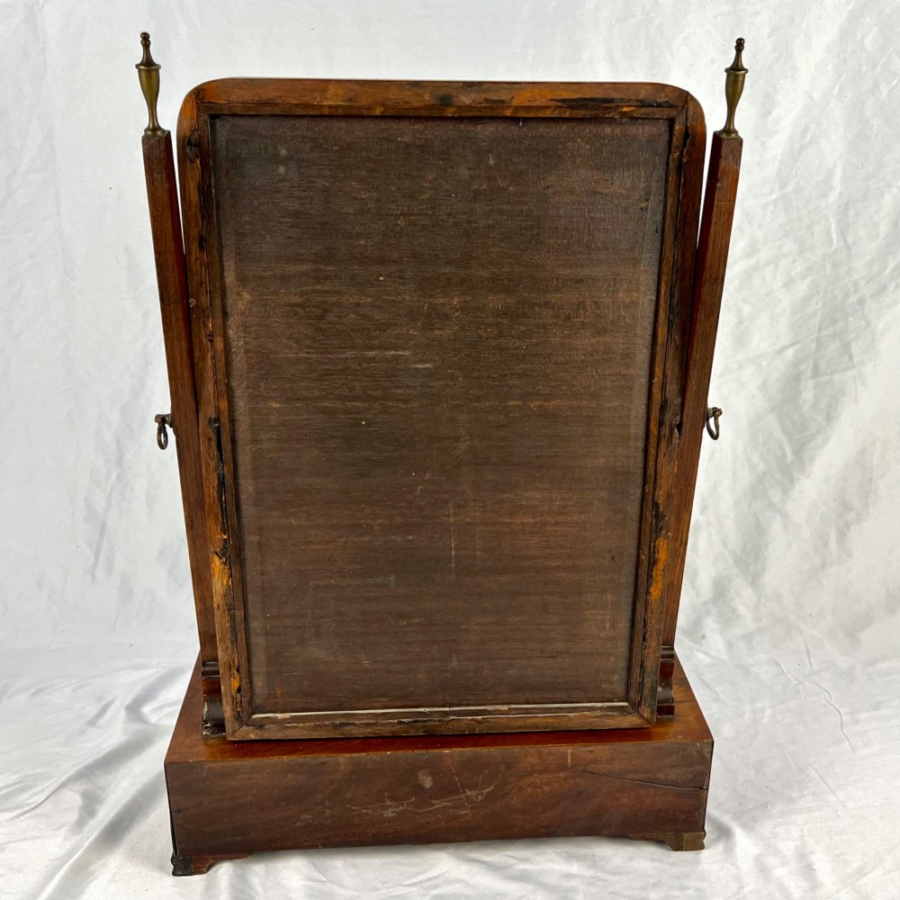 A George III mahogany toilet dressing mirror featuring an upright rectangular swing mirror flanked by brass finials, mounted on a serpentine-front base with three small drawers. View X