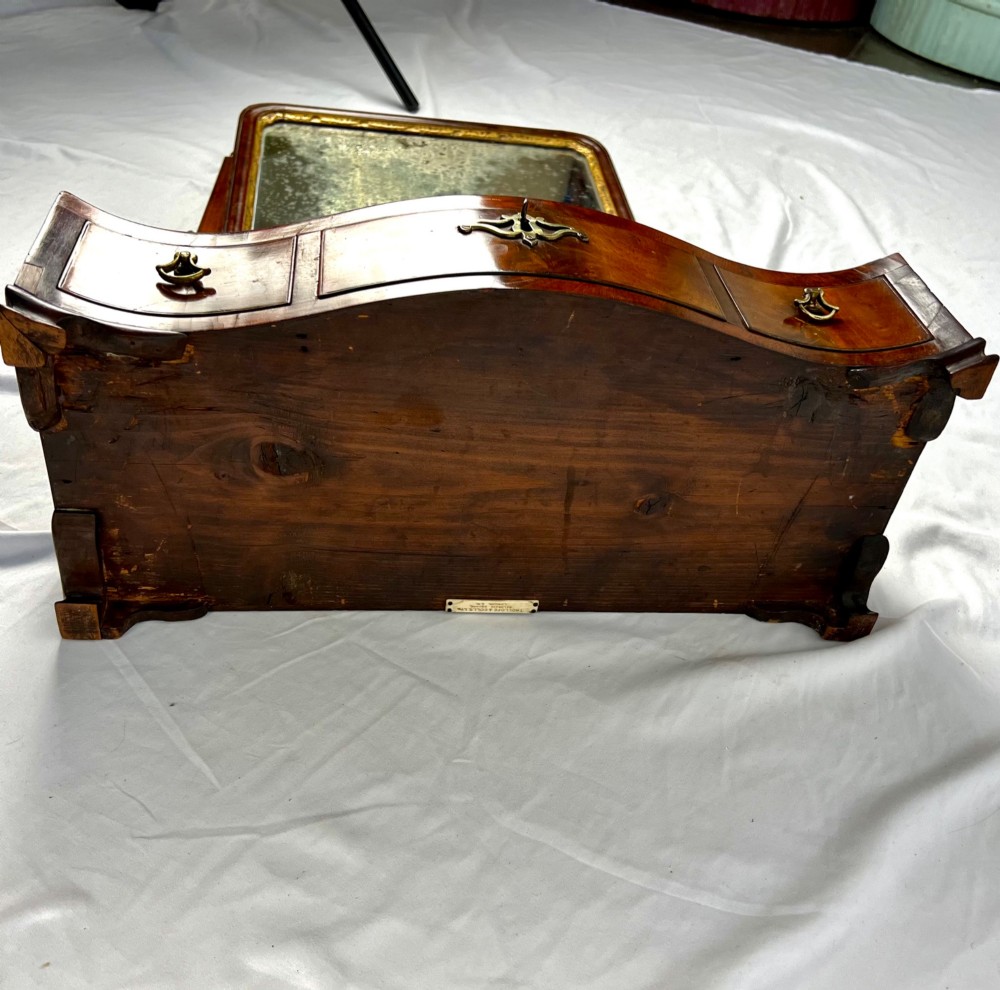 A George III mahogany toilet dressing mirror featuring an upright rectangular swing mirror flanked by brass finials, mounted on a serpentine-front base with three small drawers. View XI