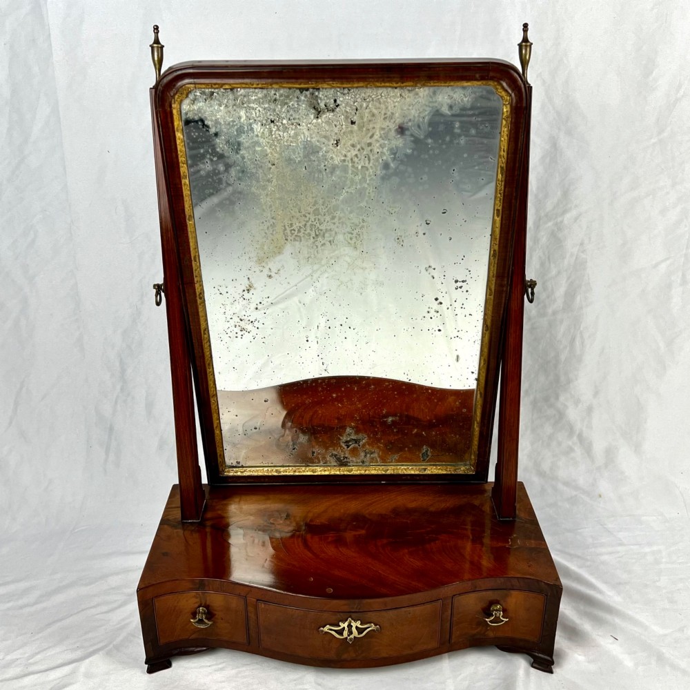 A George III mahogany toilet dressing mirror featuring an upright rectangular swing mirror flanked by brass finials, mounted on a serpentine-front base with three small drawers. View XIII
