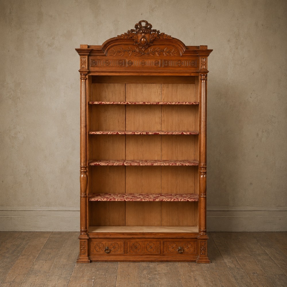A tall 19th-century Continental open wooden bookcase featuring an ornate carved pediment, fluted side columns, panelled back, and multiple adjustable shelves.