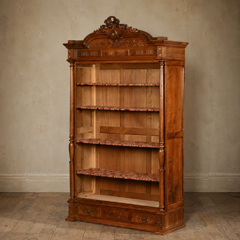 A tall 19th-century Continental open wooden bookcase featuring an ornate carved pediment, fluted side columns, panelled back, and multiple adjustable shelves. View VI