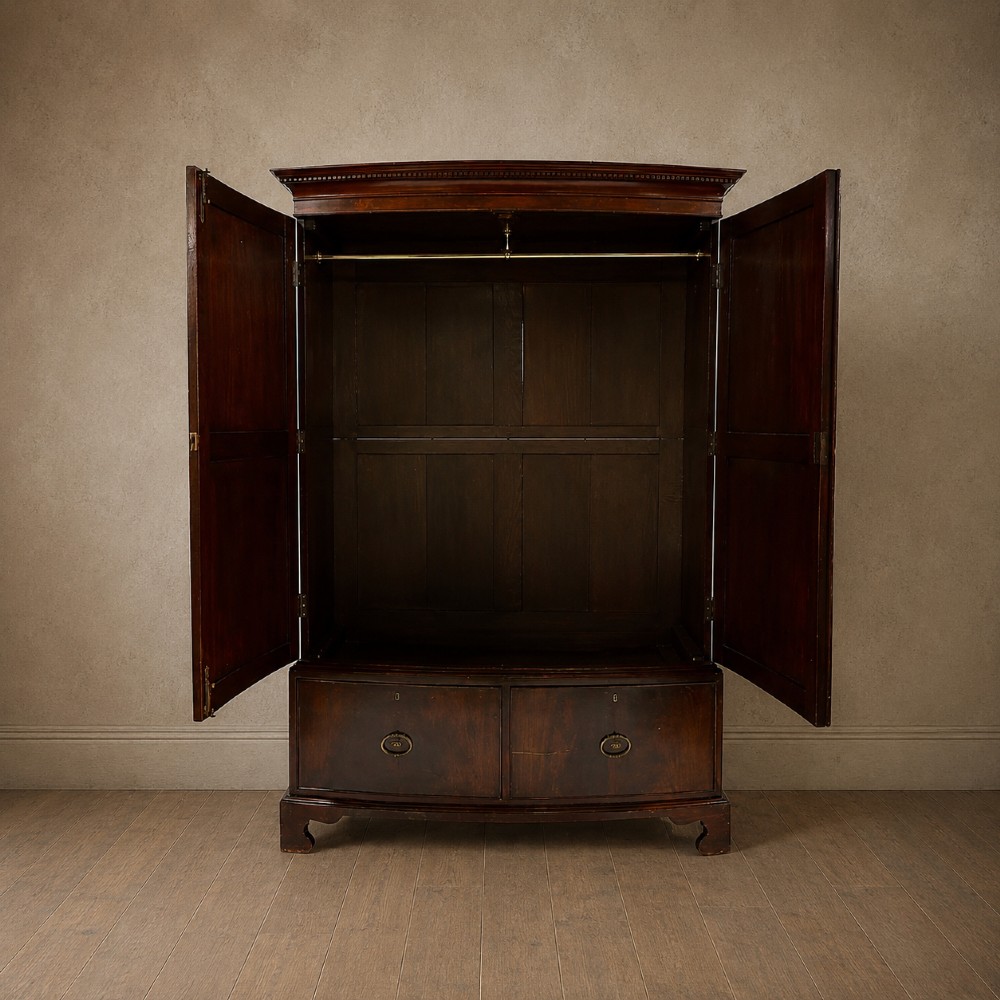 A George III bowfront mahogany wardrobe featuring twin panelled doors with oval flame mahogany veneers above two drawers and flared bracket feet. View VII