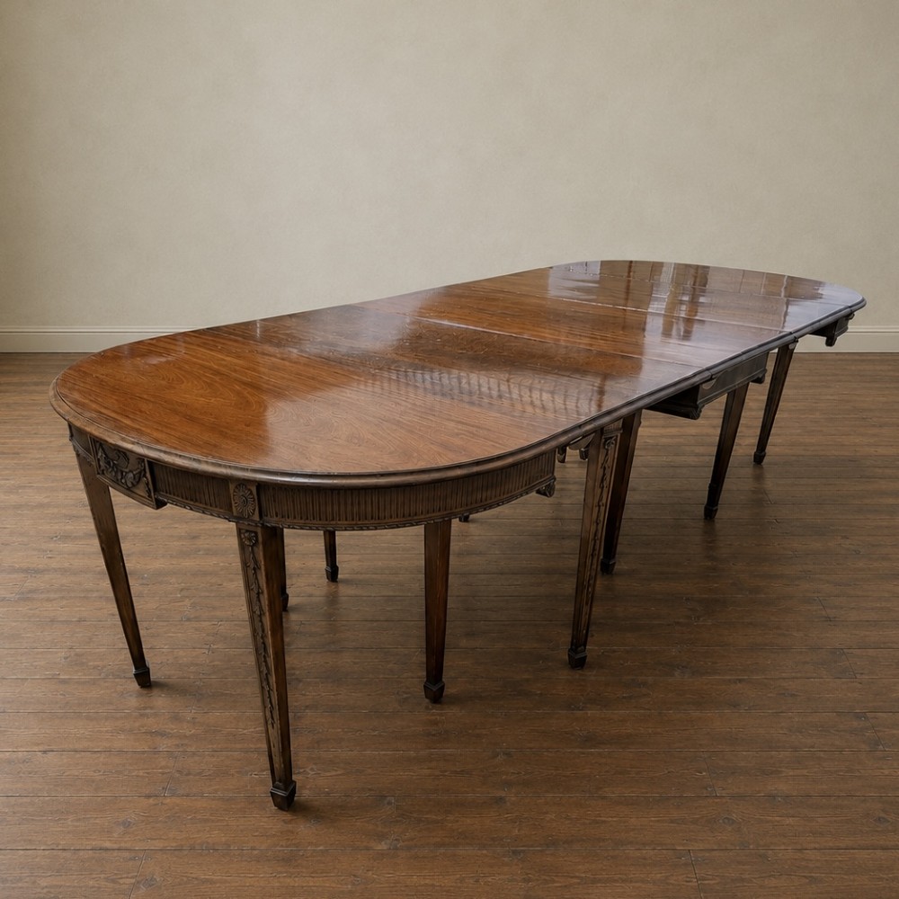 A long late George III mahogany extending dining table with D-shaped end sections, fluted friezes, carved paterae, and square tapered legs.