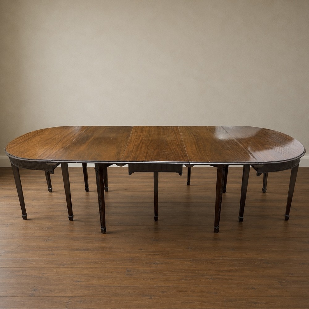 A long late George III mahogany extending dining table with D-shaped end sections, fluted friezes, carved paterae, and square tapered legs. View XI