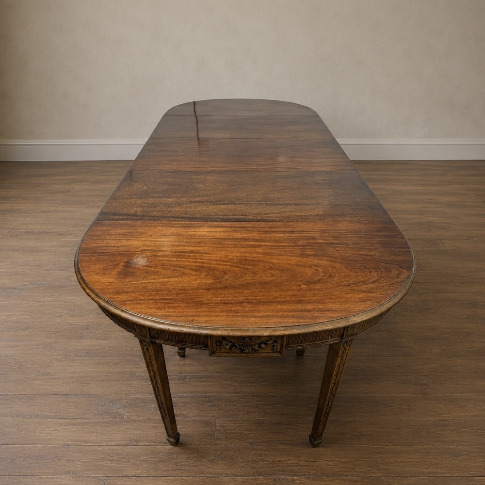 A long late George III mahogany extending dining table with D-shaped end sections, fluted friezes, carved paterae, and square tapered legs. View XII