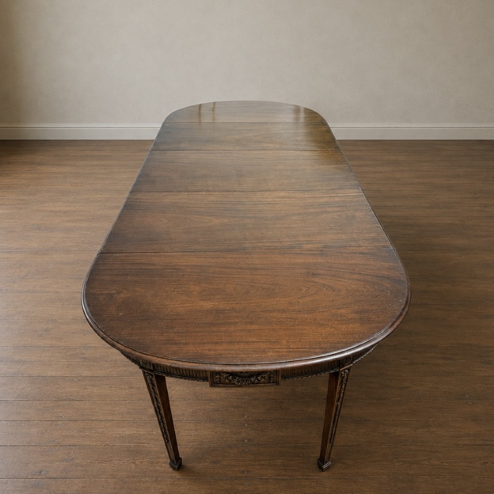 A long late George III mahogany extending dining table with D-shaped end sections, fluted friezes, carved paterae, and square tapered legs. View XIII