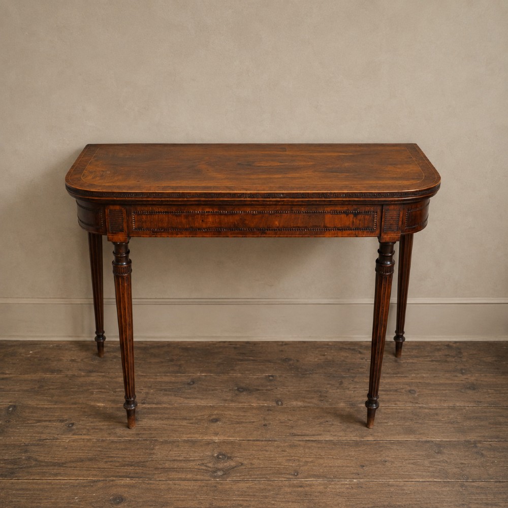 An antique Regency rosewood fold-over card table featuring burr yew crossbanding, a rectangular top with rounded corners, and slender fluted tapered legs.