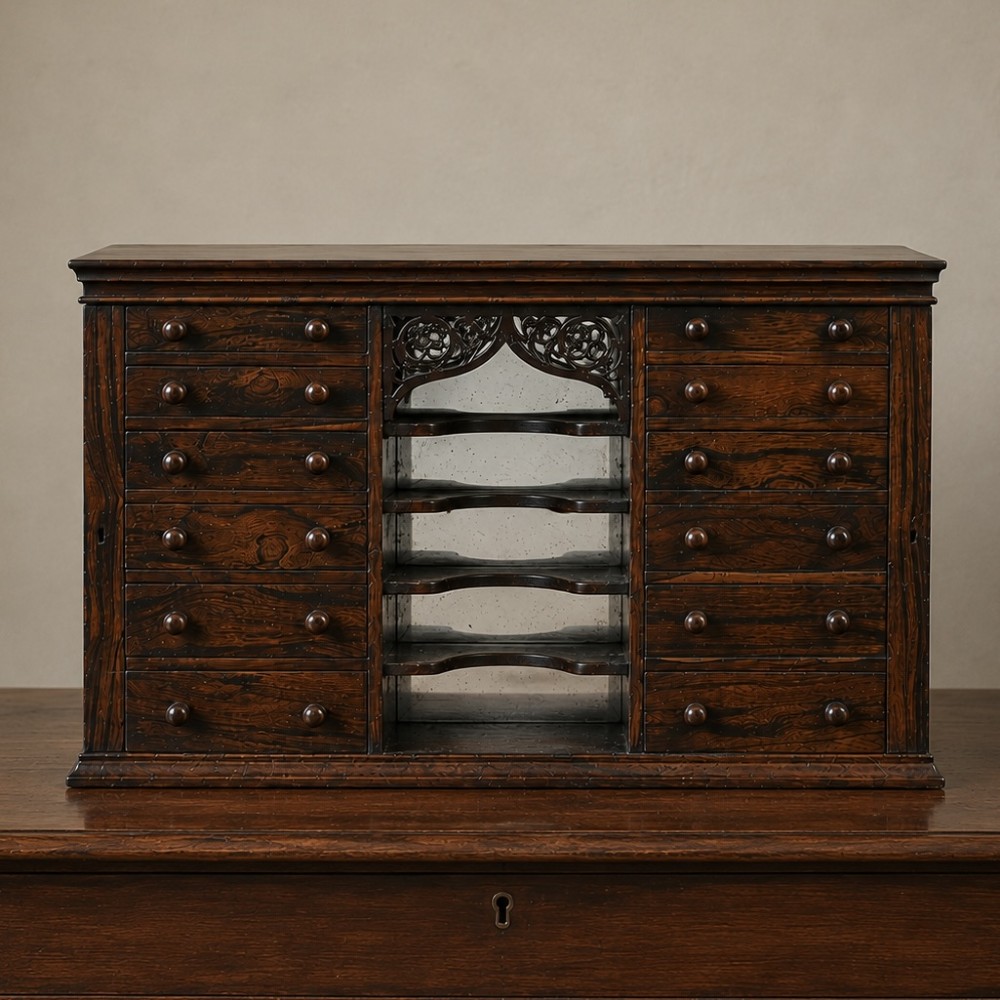 A Regency period dark rosewood tabletop collectors cabinet featuring twin banks of small drawers flanking a central mirrored shelf unit with Gothic arched carving.