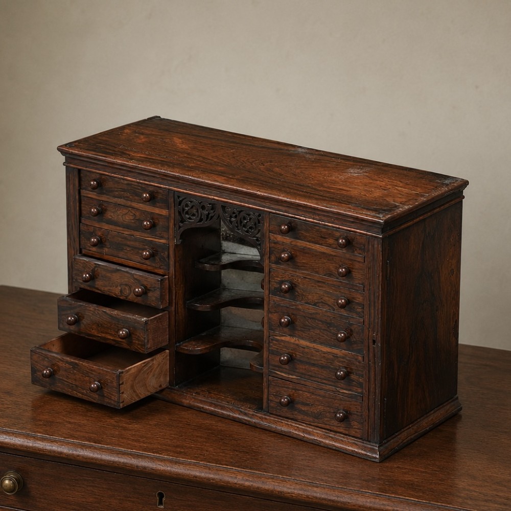 A Regency period dark rosewood tabletop collectors cabinet featuring twin banks of small drawers flanking a central mirrored shelf unit with Gothic arched carving. View IX