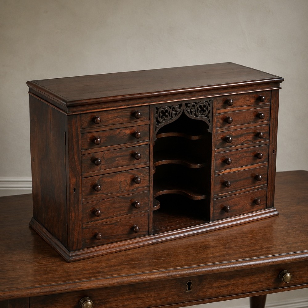 A Regency period dark rosewood tabletop collectors cabinet featuring twin banks of small drawers flanking a central mirrored shelf unit with Gothic arched carving. View XIV