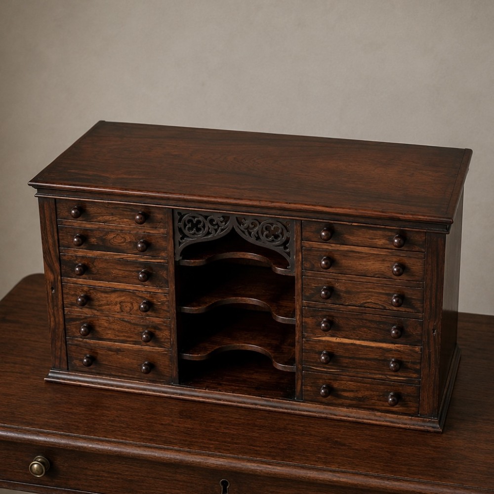 A Regency period dark rosewood tabletop collectors cabinet featuring twin banks of small drawers flanking a central mirrored shelf unit with Gothic arched carving. View XV