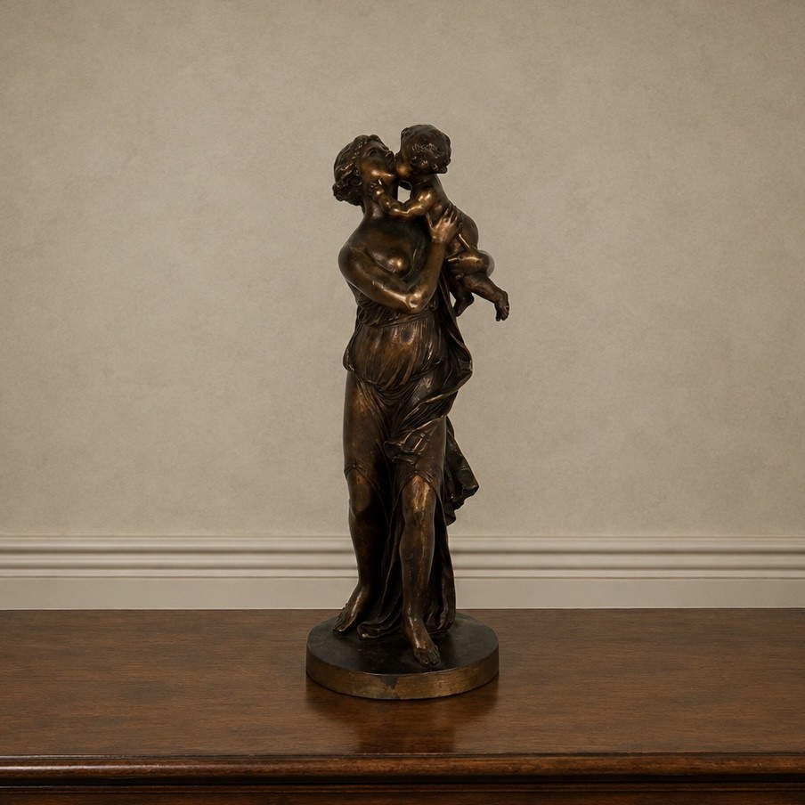 A patinated dark bronze sculpture depicting a draped classical woman holding a small child against her face, set upon a rounded bronze base.