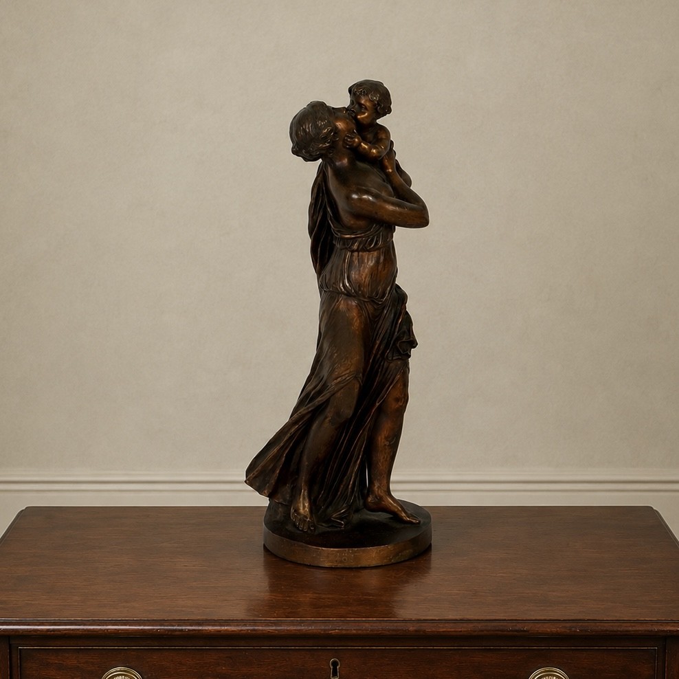 A patinated dark bronze sculpture depicting a draped classical woman holding a small child against her face, set upon a rounded bronze base. View VII