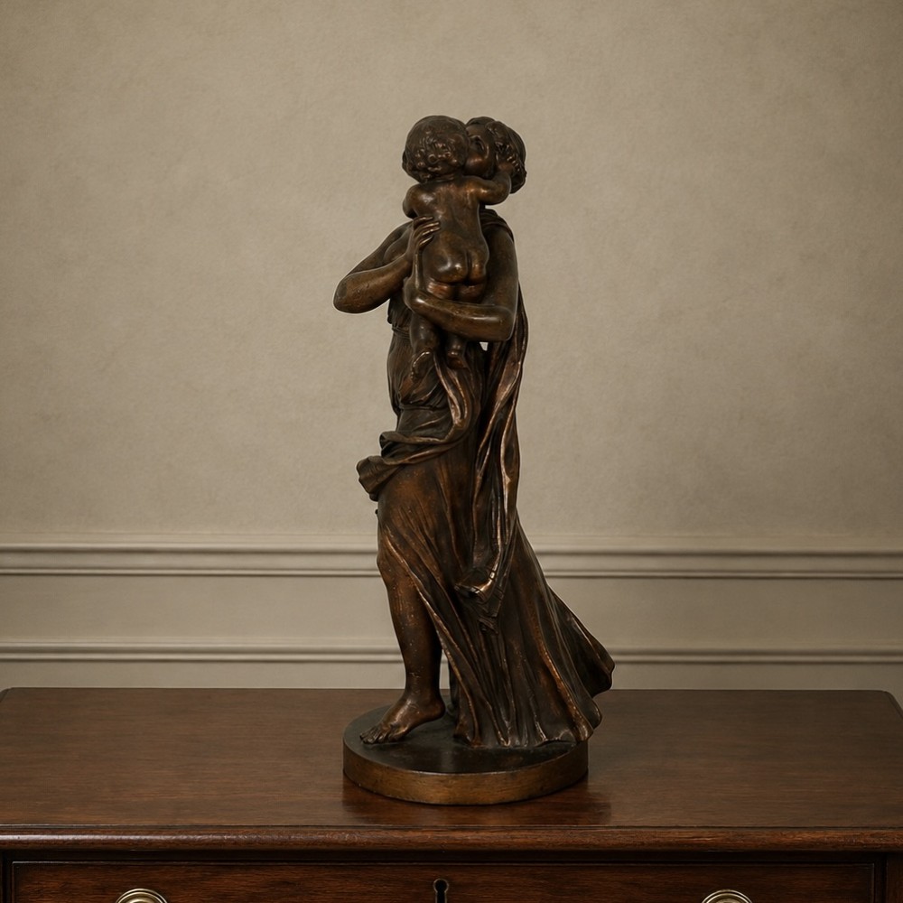 A patinated dark bronze sculpture depicting a draped classical woman holding a small child against her face, set upon a rounded bronze base. View VIII