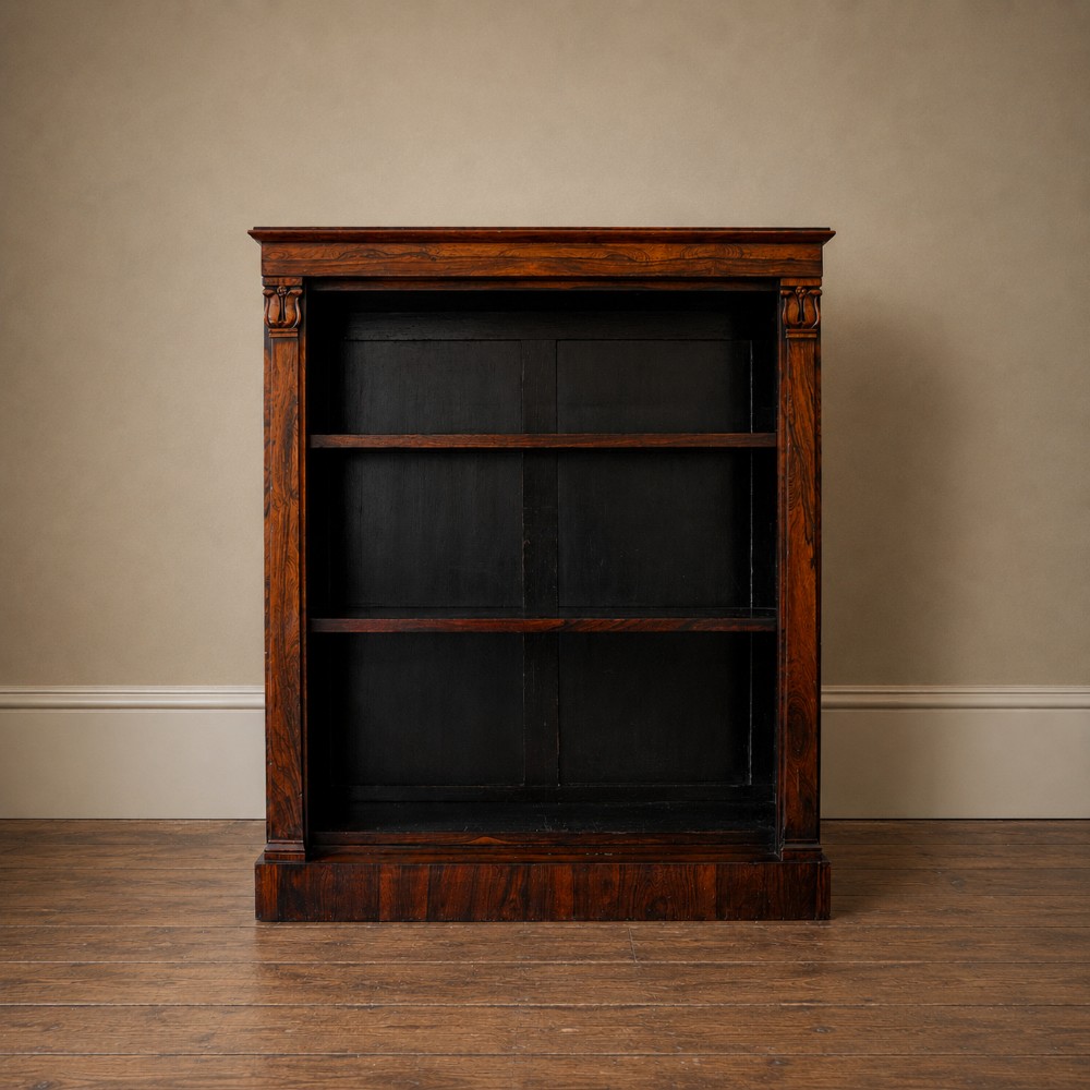 An antique William IV rosewood open bookcase featuring two adjustable shelves, a solid plinth base, and carved scroll capitals atop side pilasters.