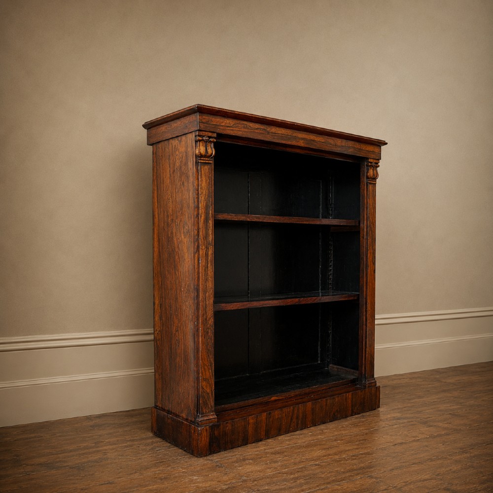 An antique William IV rosewood open bookcase featuring two adjustable shelves, a solid plinth base, and carved scroll capitals atop side pilasters. View XI