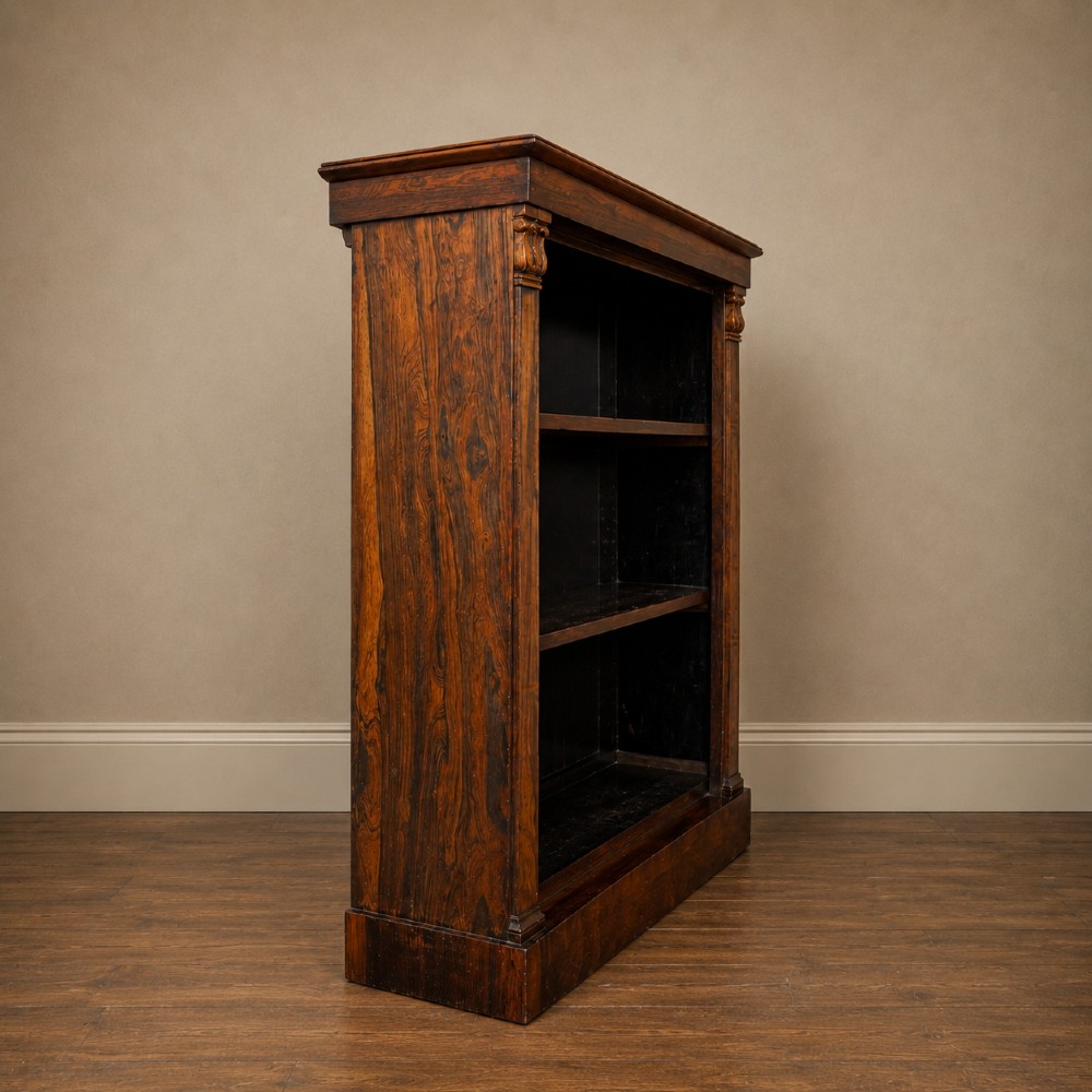 An antique William IV rosewood open bookcase featuring two adjustable shelves, a solid plinth base, and carved scroll capitals atop side pilasters. View XII