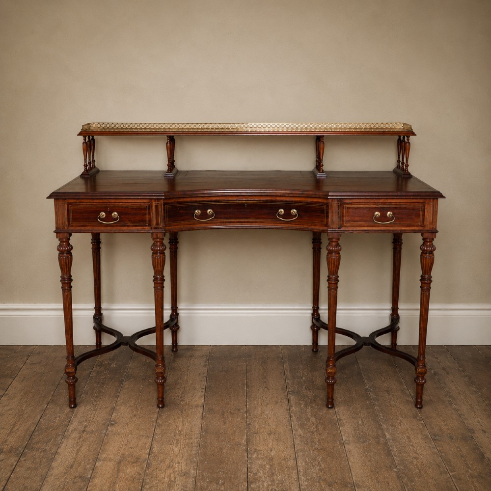 A Victorian rosewood writing desk featuring a brass gallery shelf, three drawers with brass handles, turned fluted legs, and curved stretchers.