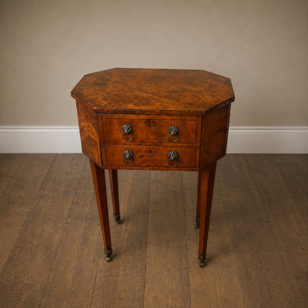 An octagonal George III satinwood work table with two drawers, lion mask ring handles, and tapered legs ending in brass castors. View VI
