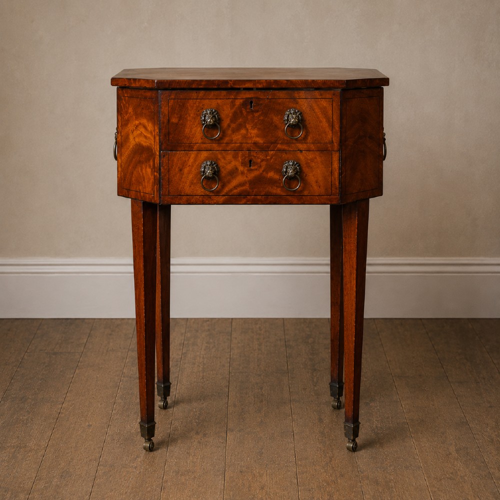 An octagonal George III satinwood work table with two drawers, lion mask ring handles, and tapered legs ending in brass castors.