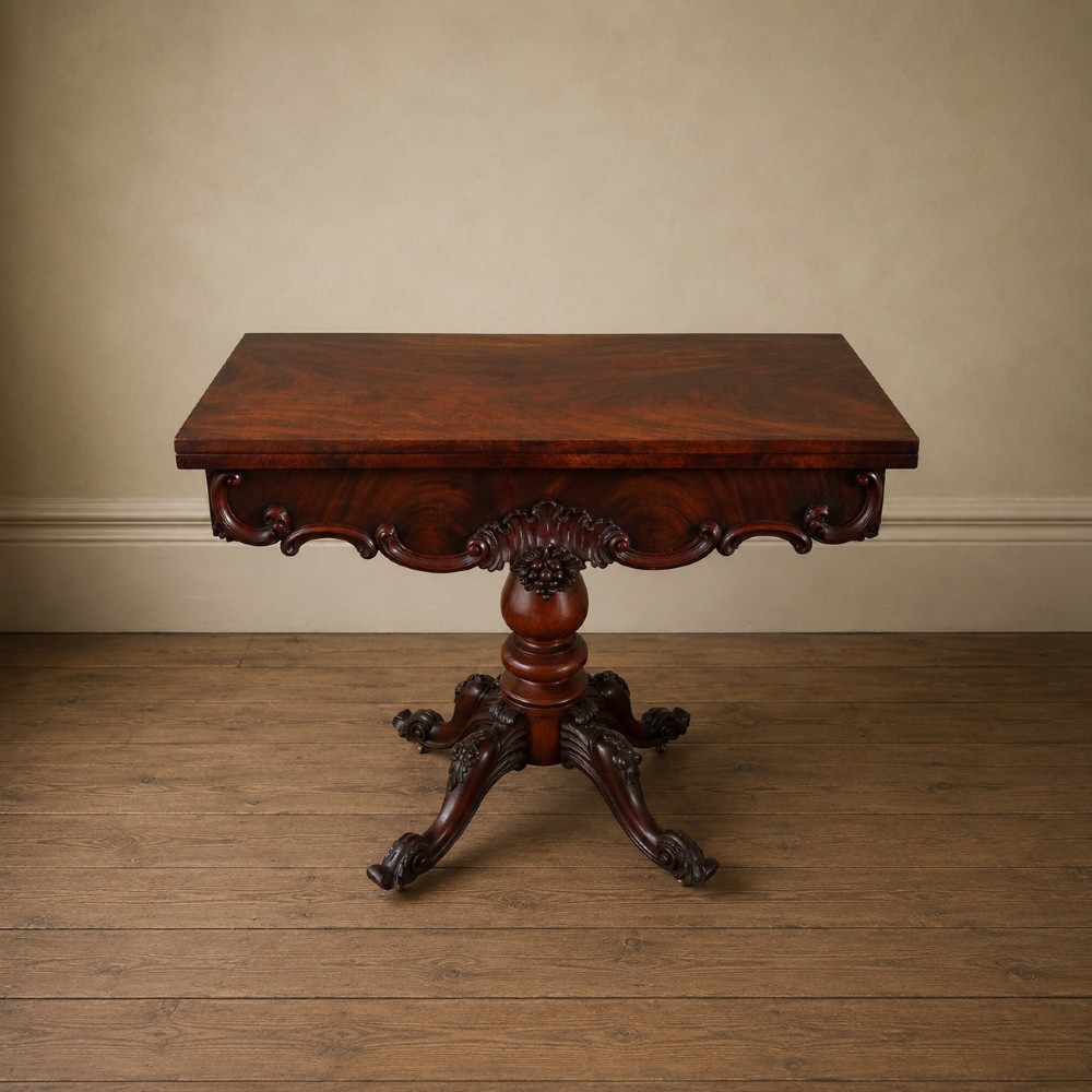 A Victorian figured mahogany card table featuring a turnover top, carved frieze, turned pedestal, and scroll legs with castors. View VII