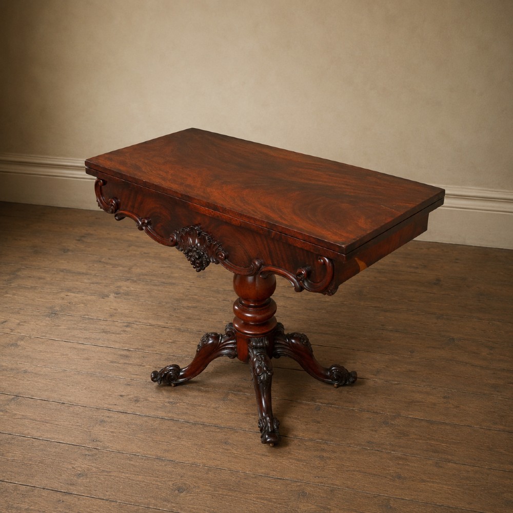 A Victorian figured mahogany card table featuring a turnover top, carved frieze, turned pedestal, and scroll legs with castors. View VIII