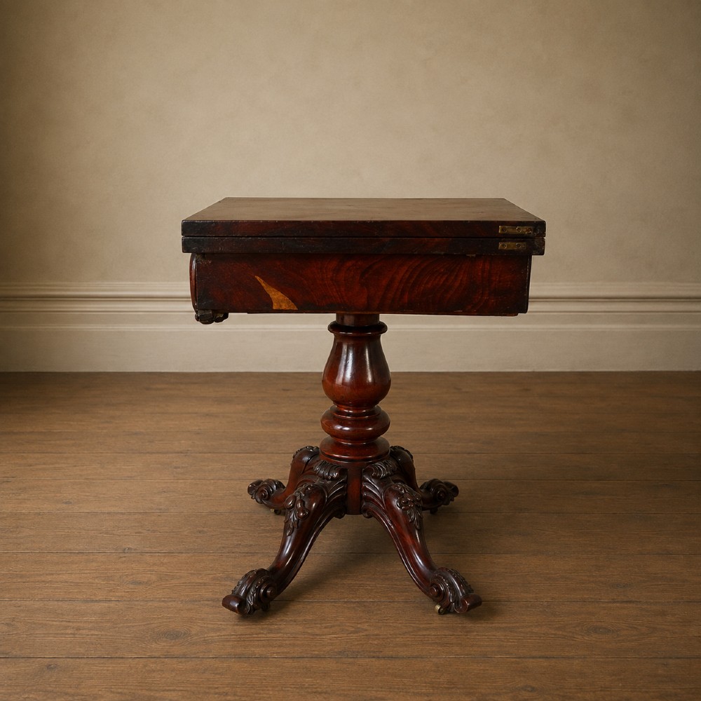 A Victorian figured mahogany card table featuring a turnover top, carved frieze, turned pedestal, and scroll legs with castors. View X