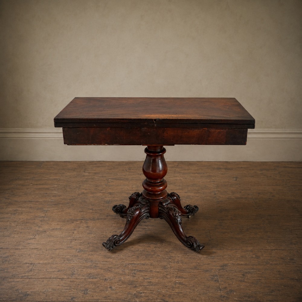 A Victorian figured mahogany card table featuring a turnover top, carved frieze, turned pedestal, and scroll legs with castors. View XI