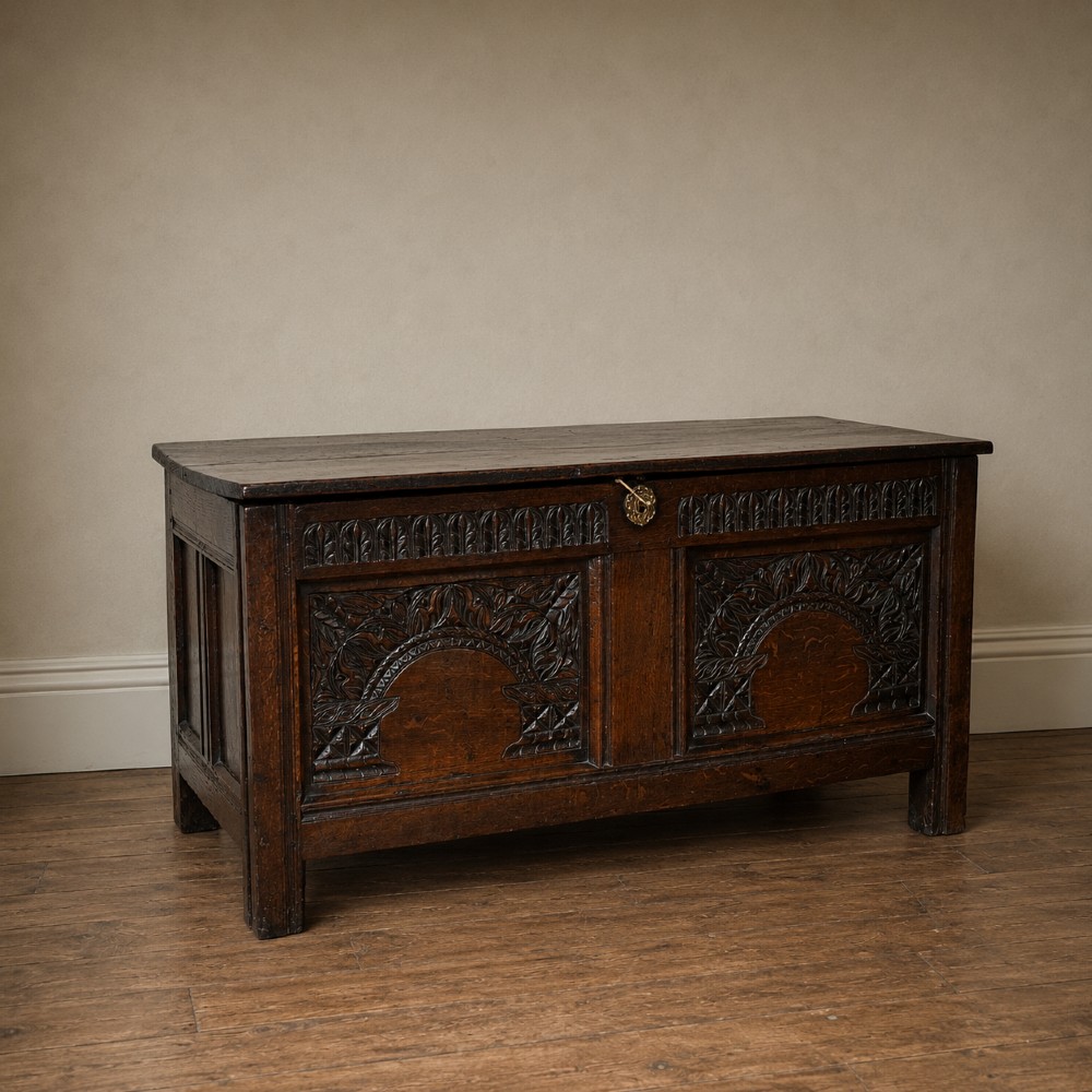 A 17th-century joined oak coffer featuring carved arch front panels, a carved top frieze, hinged lid, and brass keyhole escutcheon. View XIV