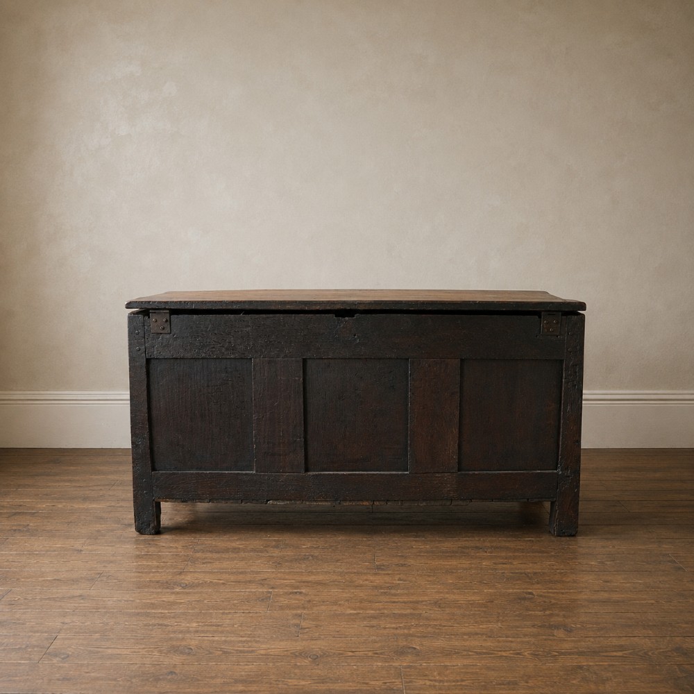 A 17th-century joined oak coffer featuring carved arch front panels, a carved top frieze, hinged lid, and brass keyhole escutcheon. View XV